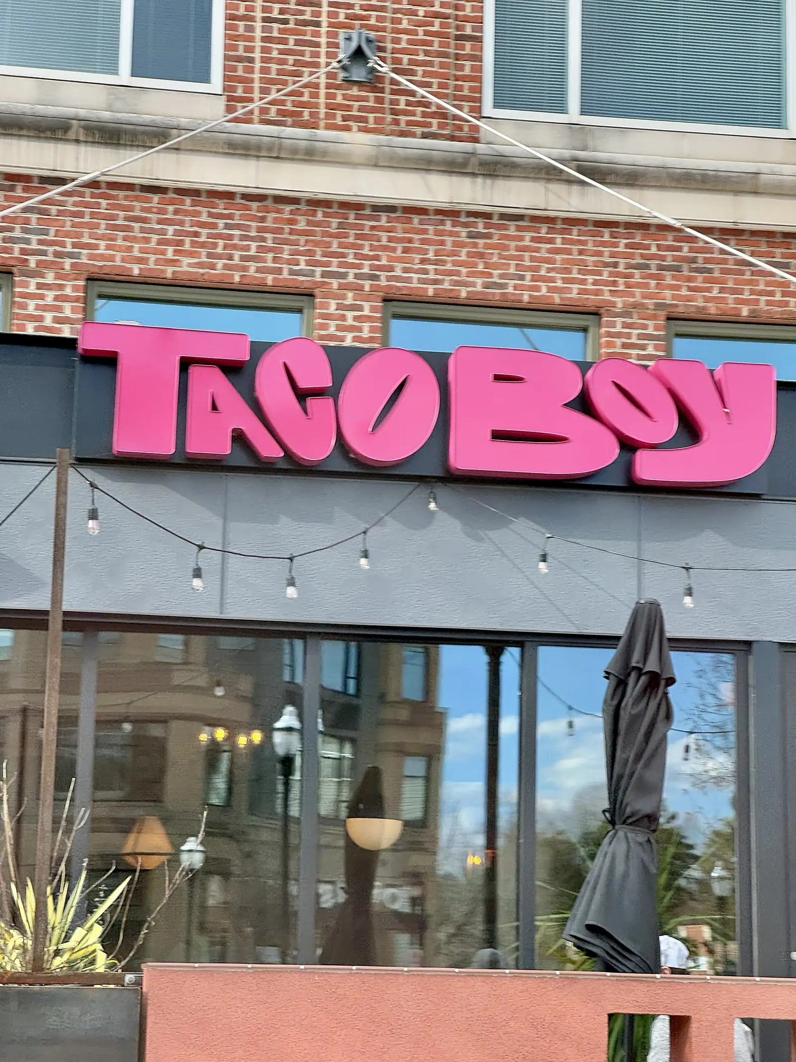 Taco Boy's sign above its patio, with string lights and a folded umbrella, on Town Square Boulevard in Biltmore Park, Asheville.